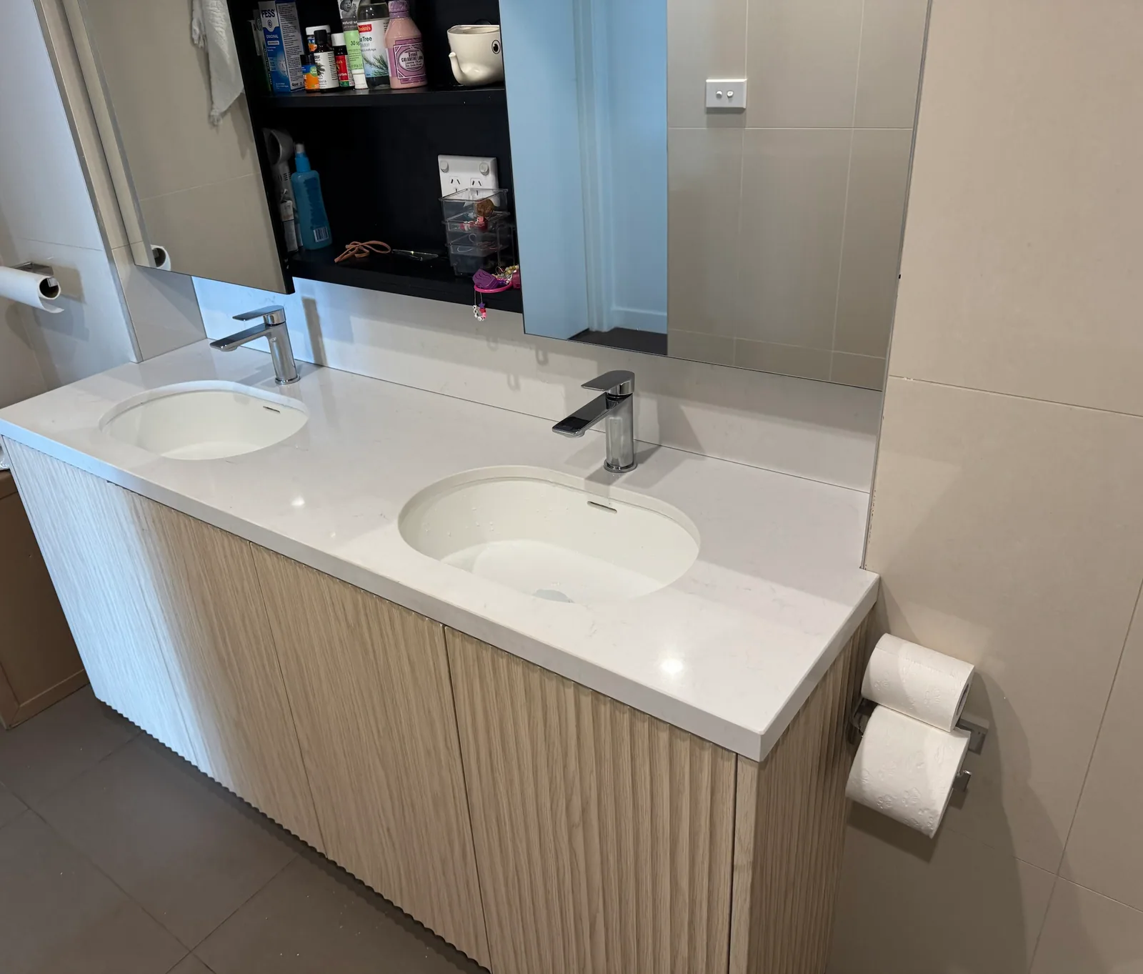 Floating fluted timber-look double vanity with stone top, two undermount basins and chrome basin mixers below a mirrored cabinet