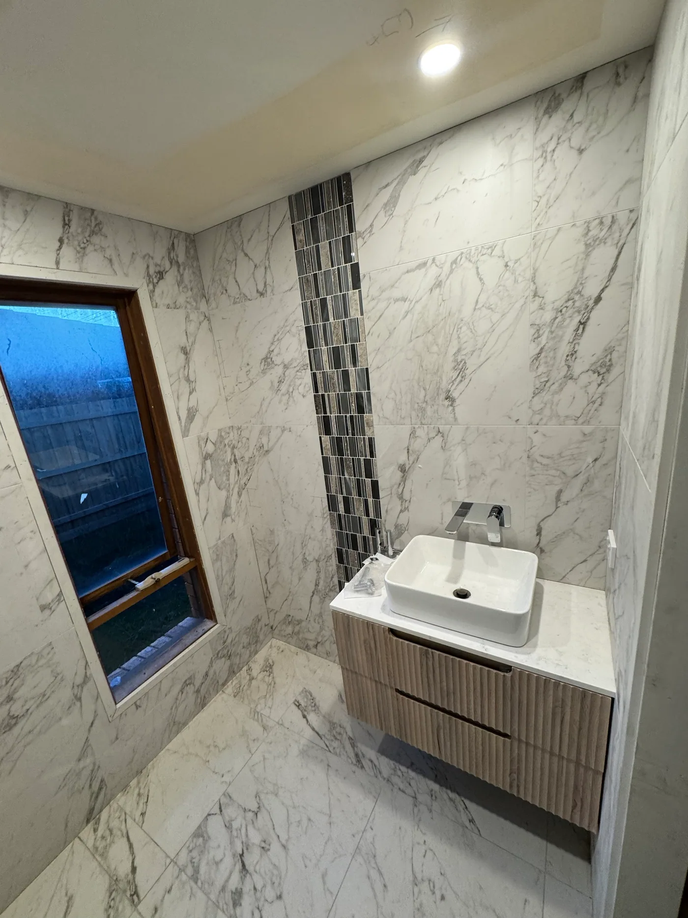 Renovated bathroom with white vessel basin on a fluted timber-look floating vanity, chrome wall mixer and marble-look wall and floor tiles